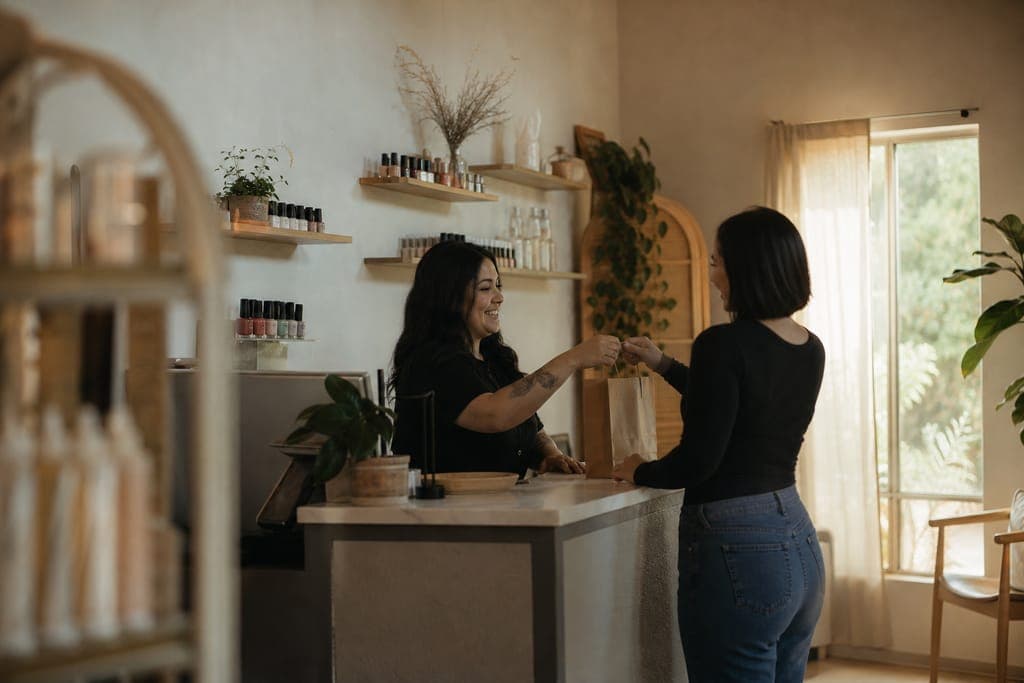 A salon stylist handing a bag to a regular client at the counter