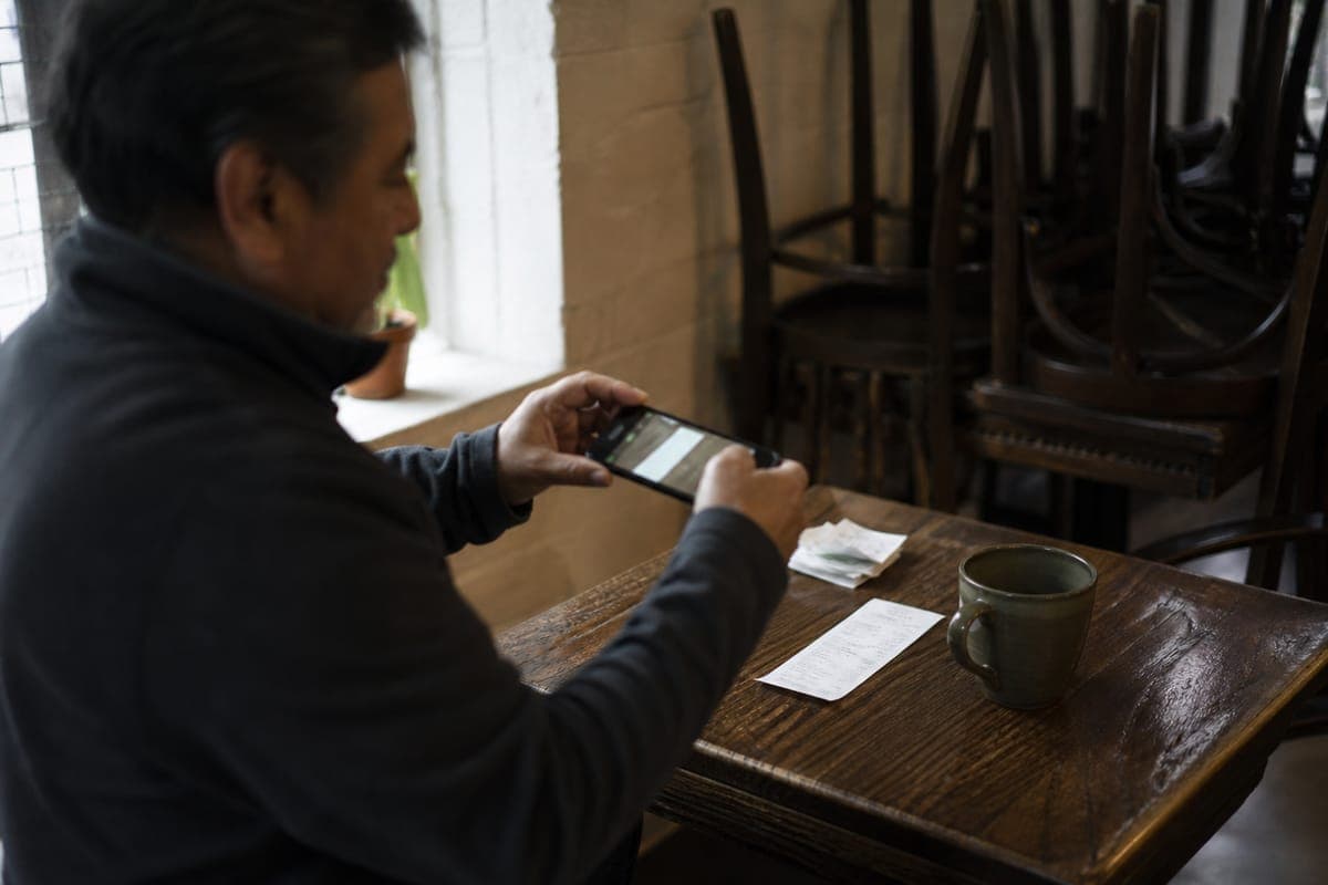 A coffee shop owner photographs a supplier receipt with his phone after closing